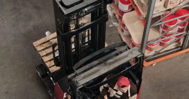 Warehouse employees discussing logistics around a forklift in an industrial setting.