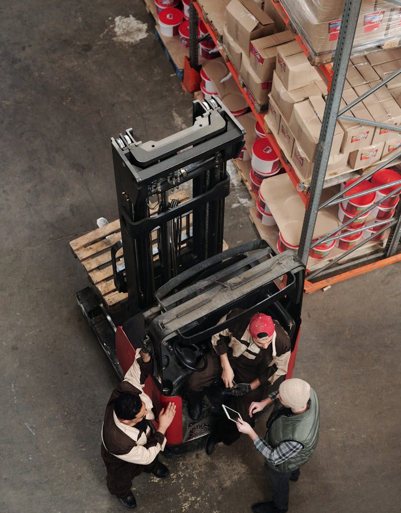 Warehouse employees discussing logistics around a forklift in an industrial setting.